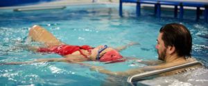 Swim coach teaching adult swimmer how to float